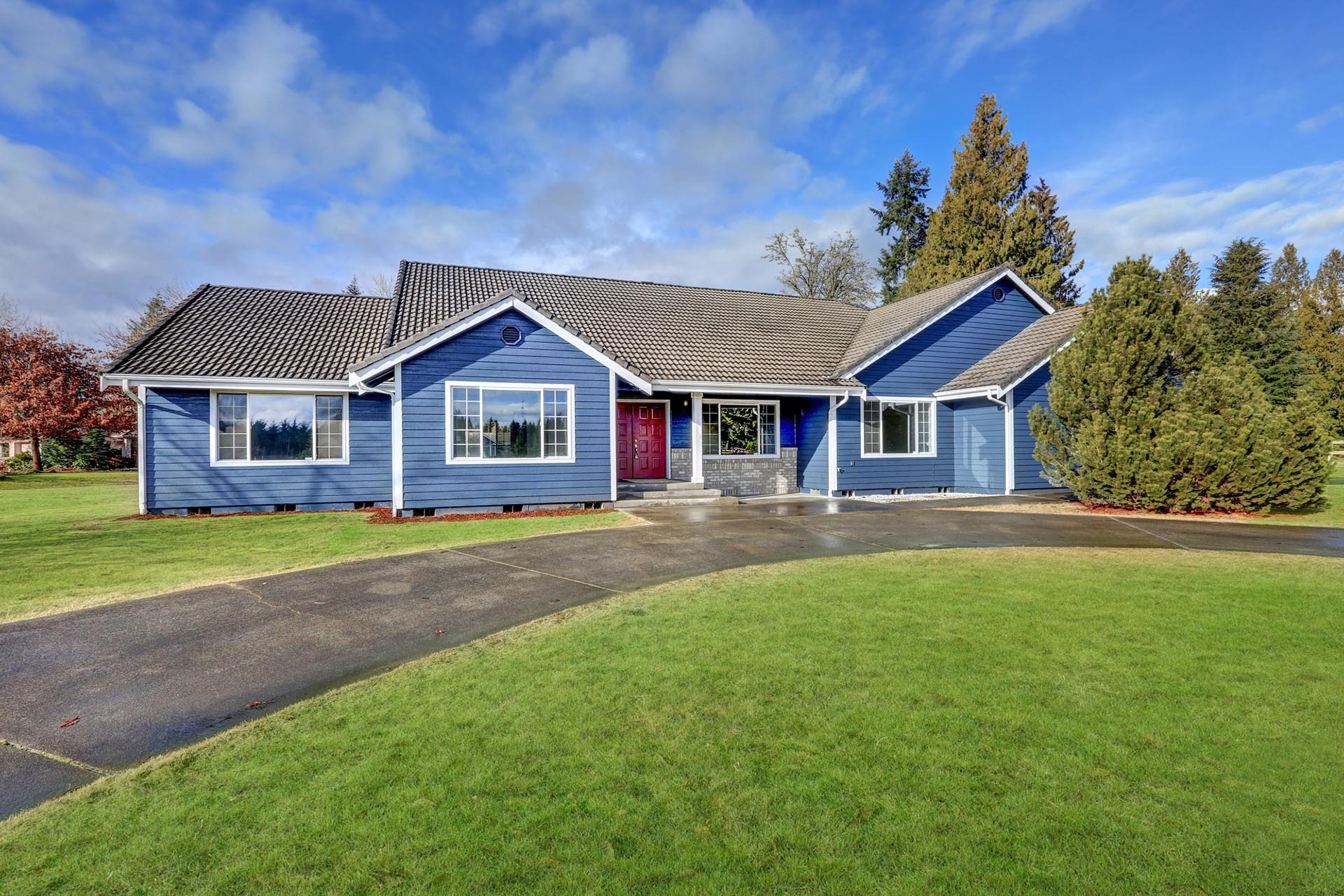 Beautiful rambler house with tile roof, blue siding, covered porch with double red front door and concrete driveway. Northwest, USA
