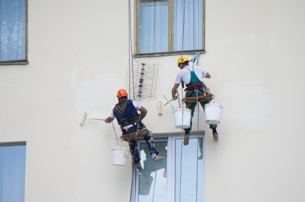 Two painters painting an exterior wall after considering the best time to paint.