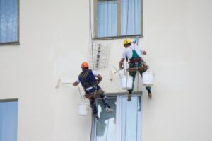 Two painters painting an exterior wall after considering the best time to paint.