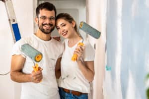 A joyful couple engaging in the task of painting their house walls, embodying the essence of teamwork and domestic bliss. The scene captures a moment of home improvement and partnership, possibly using products from the best paint brands.
