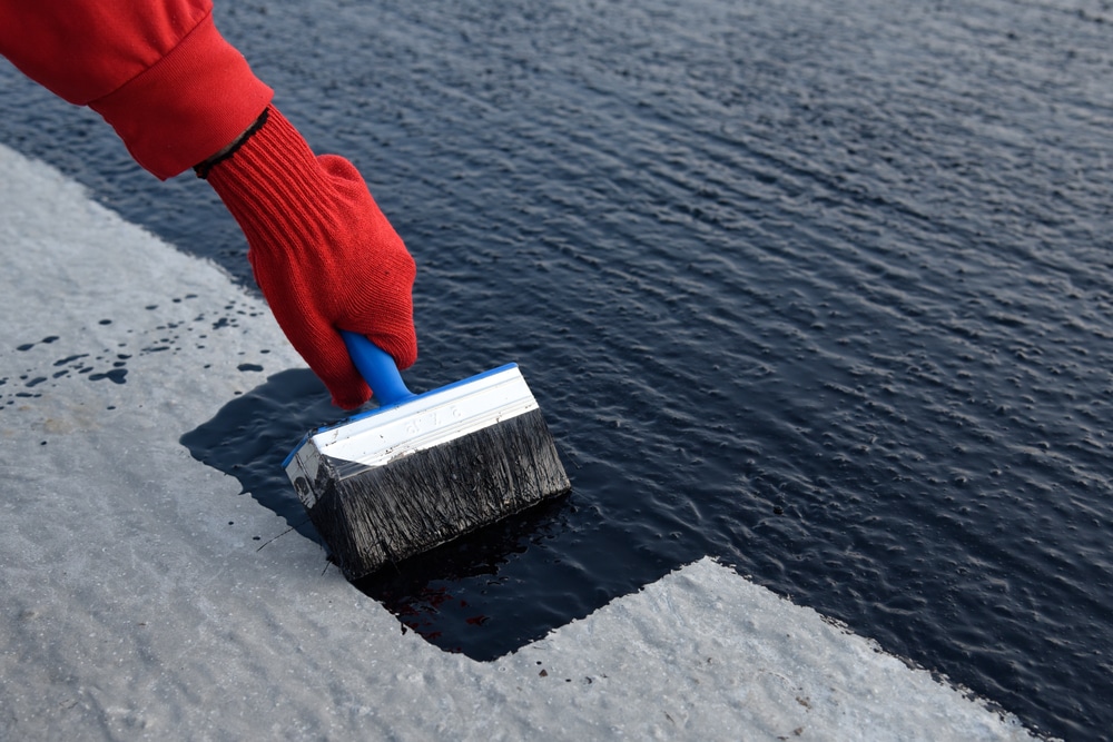 A worker applying a commercial roof painting coating with a brush on a flat roof, demonstrating the detailed work involved in roof maintenance and protection.