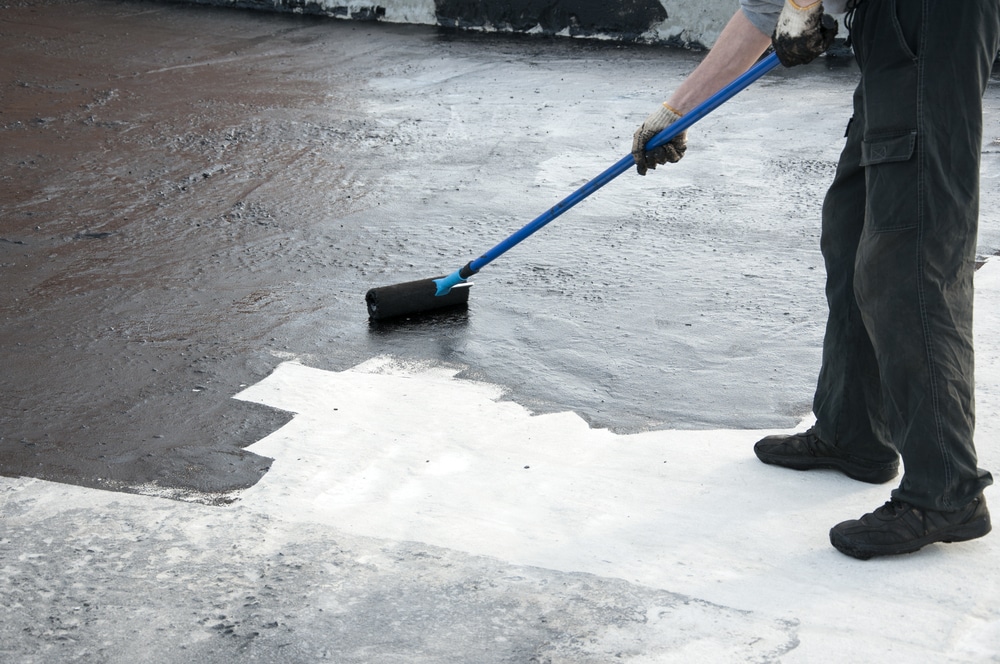 A worker applying a coating on a rooftop using a roller. This task is typical for a commercial roof painting company providing maintenance and protection services for flat roofs.