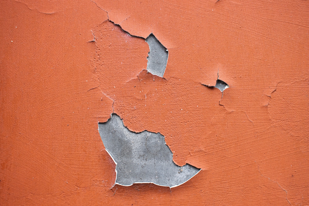 Peeling orange wall paint revealing gray surface underneath—illustrates common DIY painting problems and highlights the importance of professional surface preparation when comparing painting yourself vs hiring a painter.