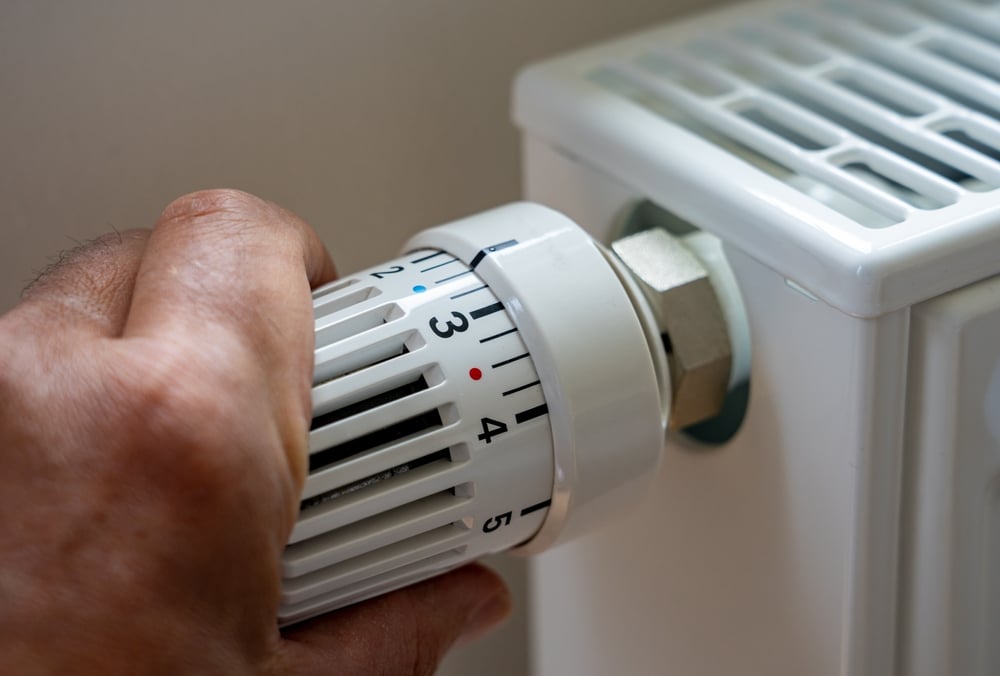 Close-up of a hand adjusting a radiator thermostat, representing the impact of temperature regulation indoors, relevant to how different shades on a paint color heat absorption chart can influence room temperature and energy efficiency.

