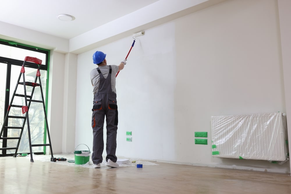 Professional painter using a roller to coat interior wall—represents quality workmanship and factors into the cost of hiring a painter for home renovations.
