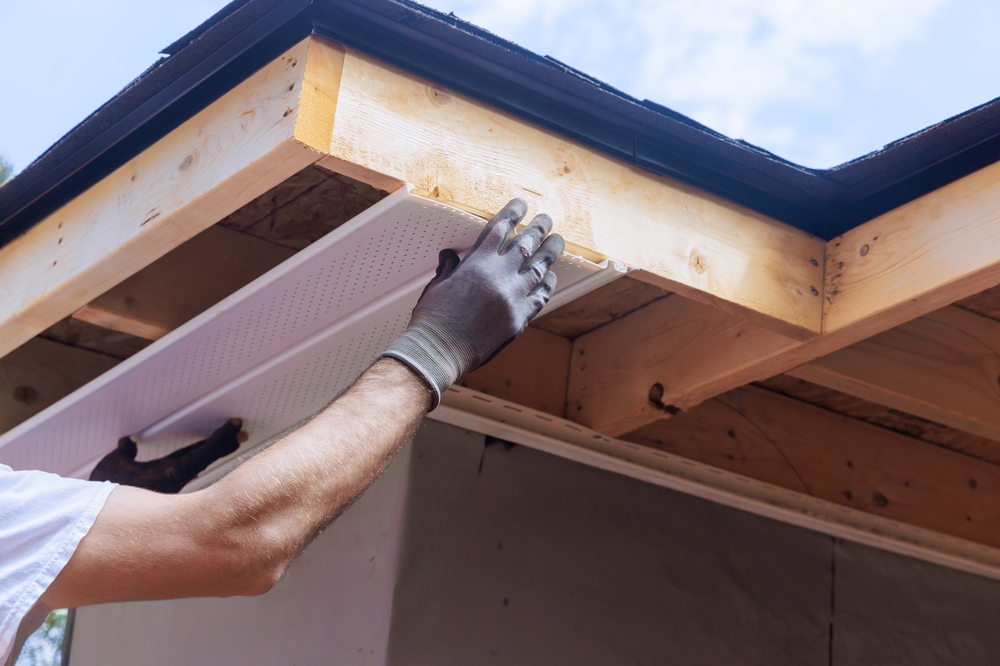 A person performs siding repair by carefully placing a new piece of material along the roofline. This task is crucial for maintaining the durability and appearance of a home's exterior.