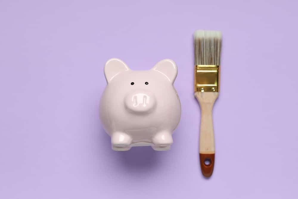 Minimalist concept showing a piggy bank and a paintbrush on a pastel purple background, symbolizing financial planning and renovation—visual metaphor related to capital improvement with painting.