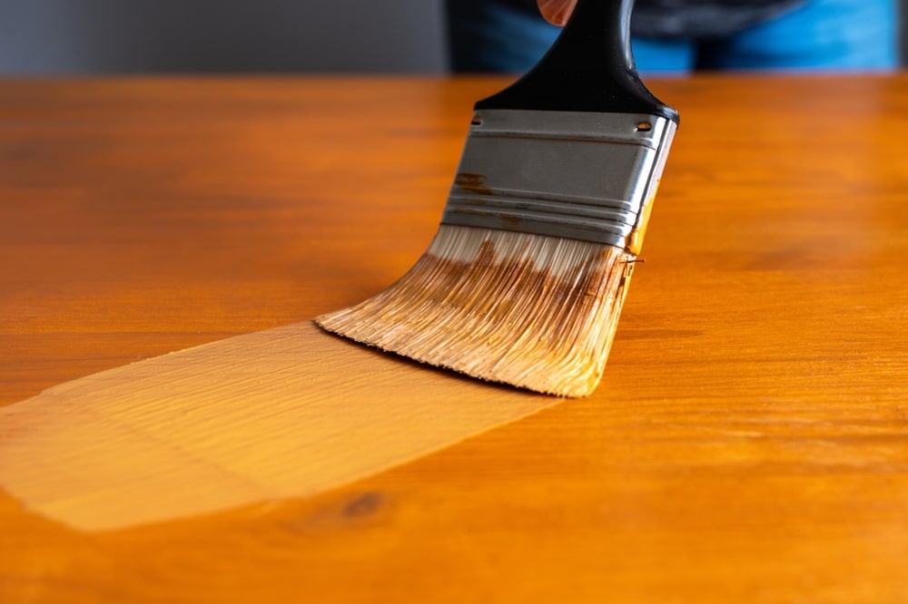 "Can you paint over stained wood without sanding? This image shows a close-up of a paintbrush applying paint directly over a stained wooden surface, illustrating the possibility of skipping the sanding step.