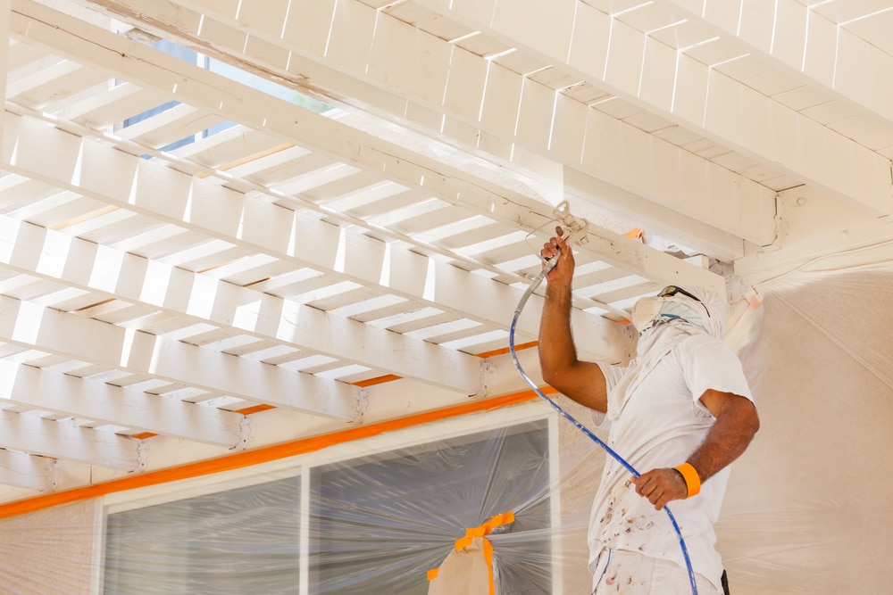  professional demonstrates how to prep a deck for painting by using protective coverings and spray equipment, showing that expert preparation leads to a flawless finish.