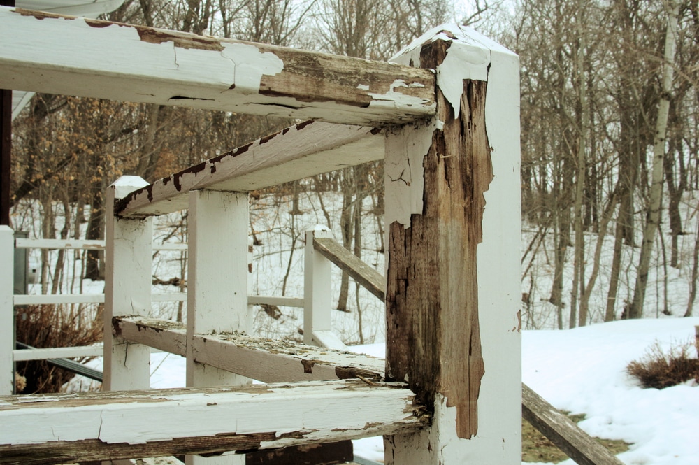 Old peeling paint on a wood railing in winter, showing surface damage—example of why learning how to repaint a wood deck is essential.