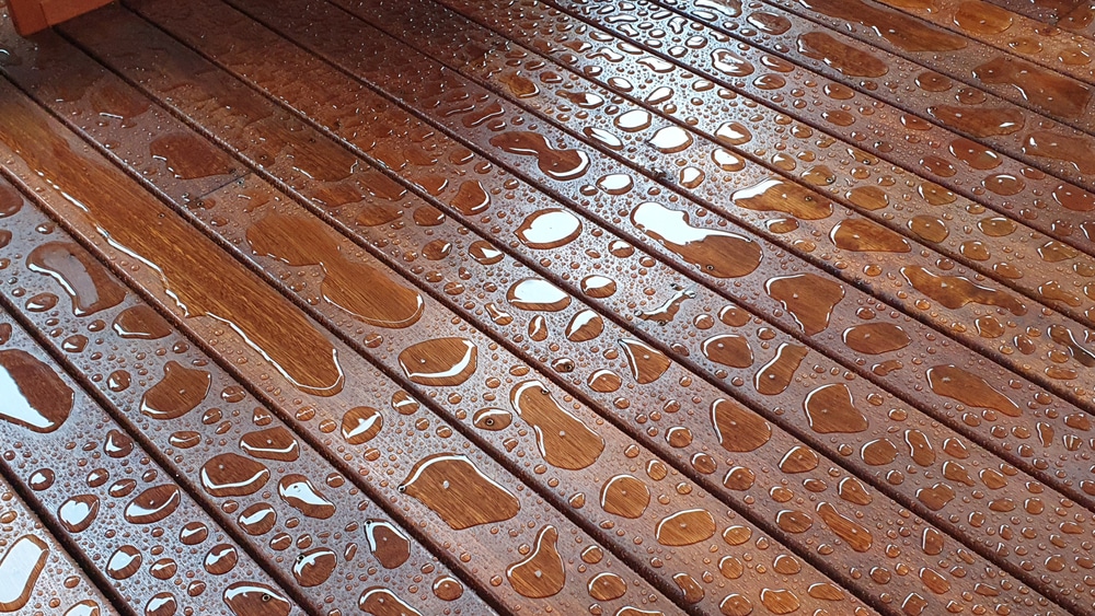 Close-up of wet wood deck with water droplets—illustrating what happens if you don't wait long enough after staining; raises the question: how long does stain take to dry?
