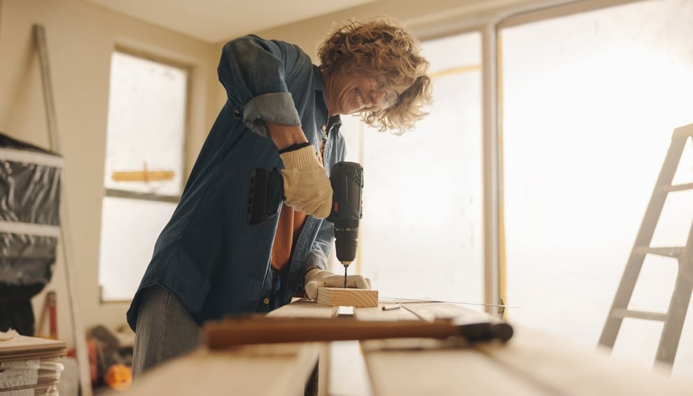Woman using a power drill while working on a DIY project indoors, representing hands-on home improvement ideas and creative renovation efforts.