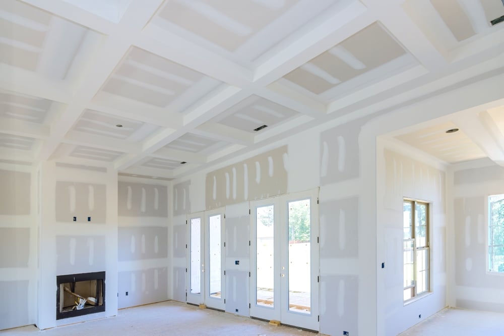 Interior view of a house under construction with unfinished drywall, coffered ceilings, and natural light—capturing a home remodel in progress.
