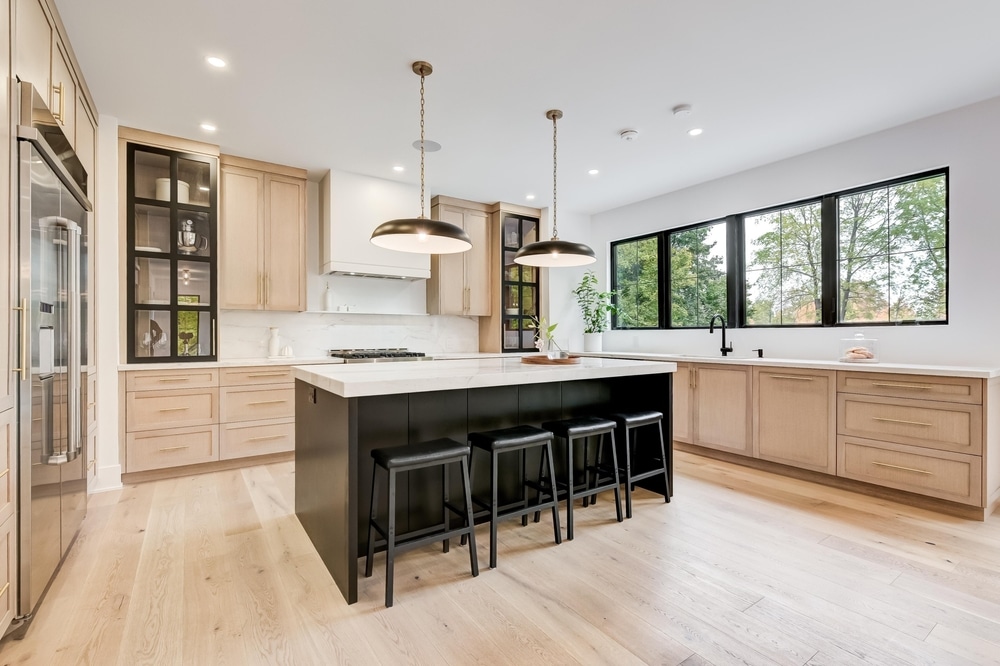 Modern kitchen with light wood cabinetry, black island with bar stools, and large windows—showcasing a stylish home renovation focused on functionality and aesthetics.