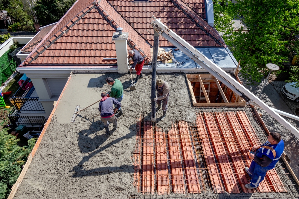 Construction crew pouring concrete on a rooftop, a major structural upgrade often included in a checklist for home renovation projects.