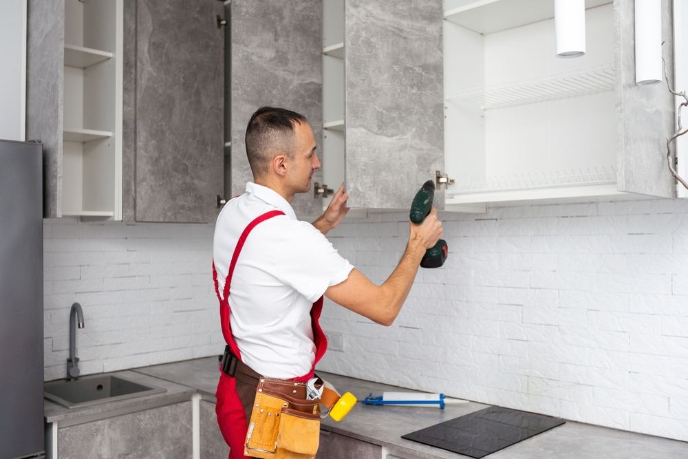 Contractor installing upper kitchen cabinets with a drill, representing a key step in a Home Renovation Checklist for interior upgrades.