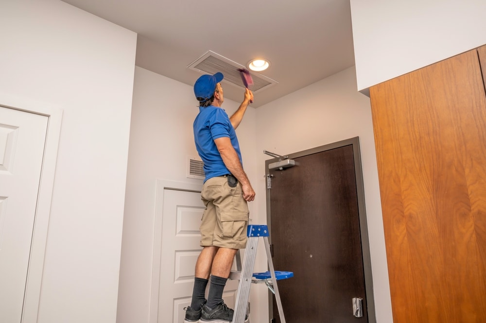 Man standing on a step ladder cleaning an air vent inside a home representing maintenance tasks that can affect home improvement return on investment.