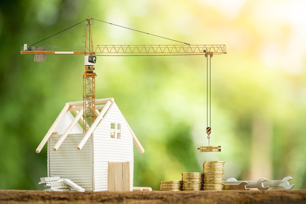 Miniature house under construction beside stacks of coins, with a crane lifting money — concept for “can you write off home repairs on your taxes?”