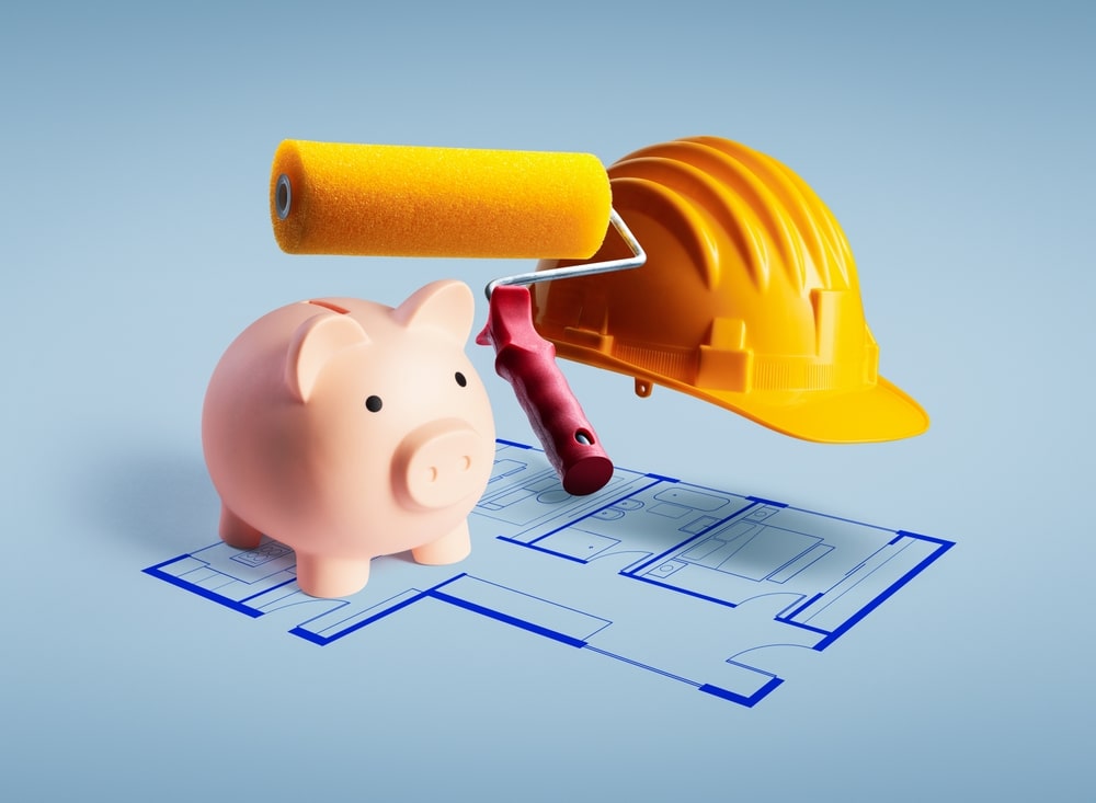 Piggy bank, paint roller, and construction helmet on top of house blueprints, symbolizing budgeting and planning for a home improvement tax deduction.