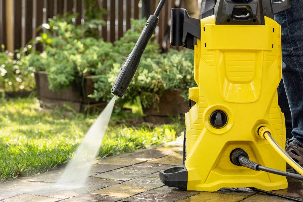 Close-up of a yellow pressure washer blasting cold water to consider pressure washing prices.
