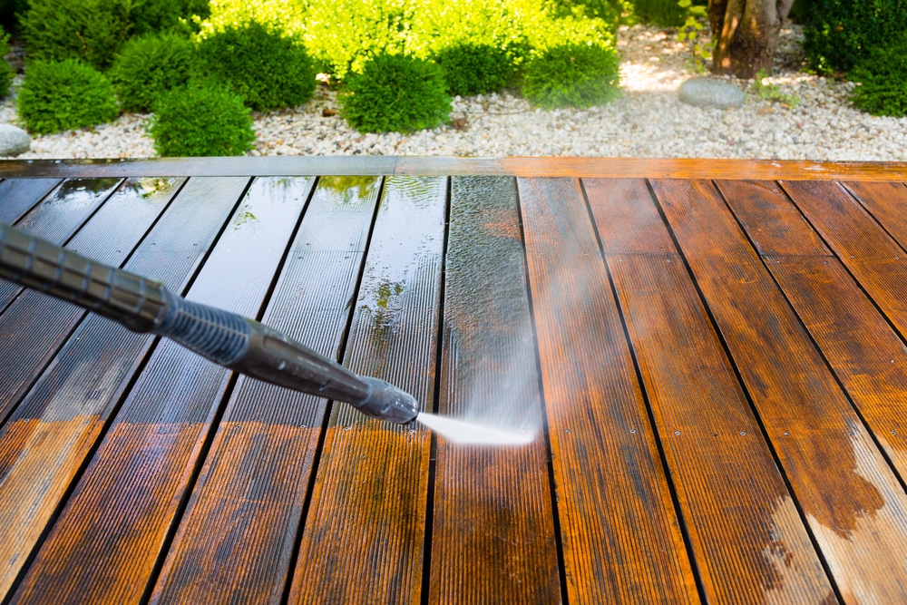 Close-up of a power washer cleaning a wooden deck, showing the best time to power wash a house for seasonal maintenance and curb appeal.