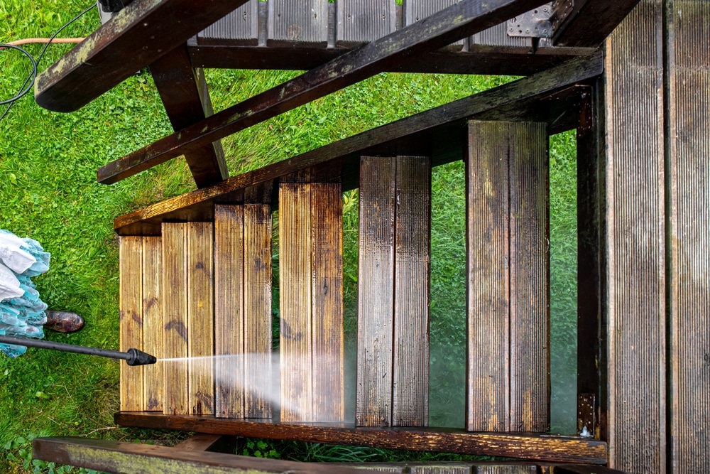 Close-up of a person cleaning wooden outdoor stairs with a power washer, showing before and after results; perfect example for pressure washing tips to restore wood surfaces.