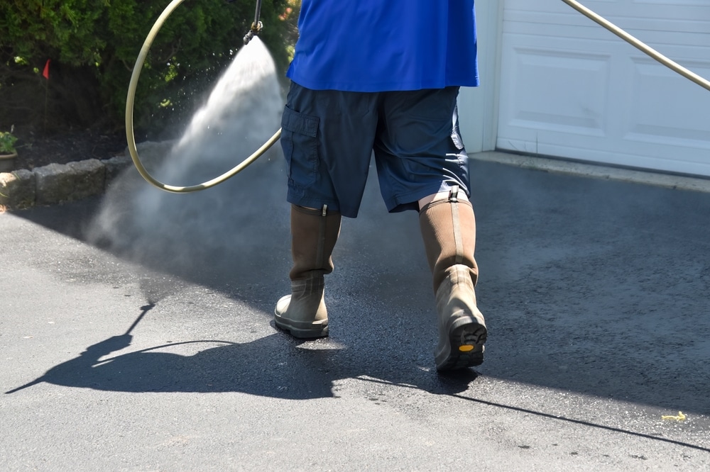 A person pressure washing a concrete driveway with a high-pressure hose, cleaning the surface. This method raises the question: can pressure washing damage concrete?