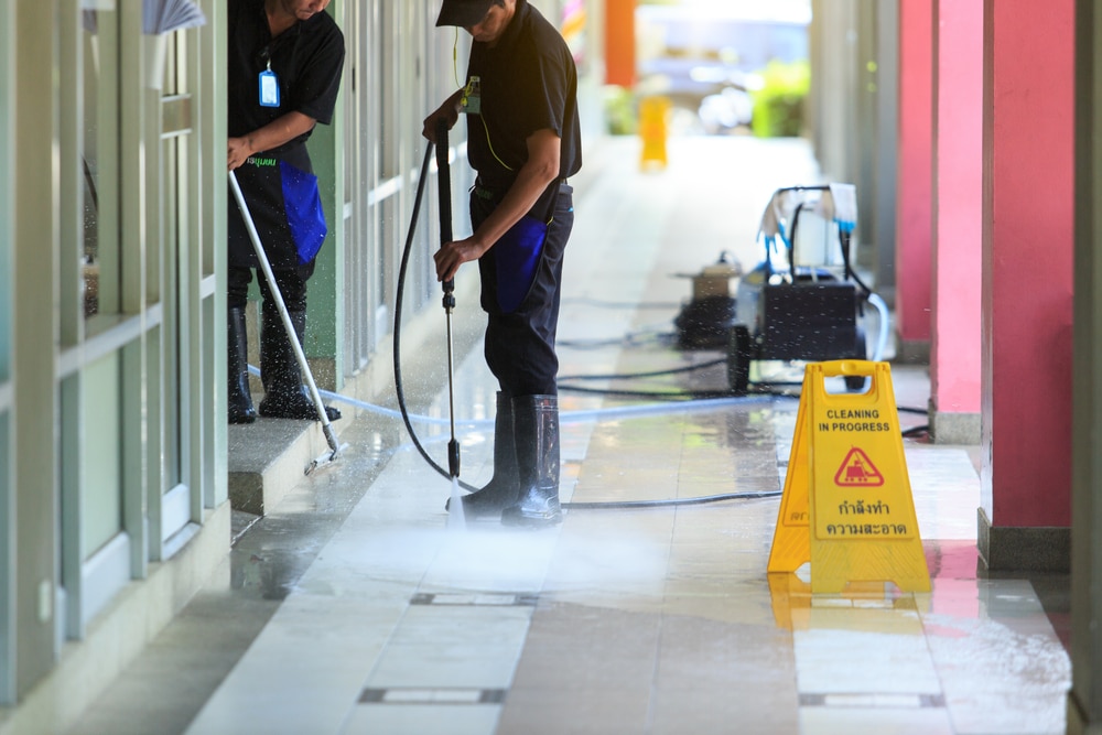 Workers providing professional pressure washing services to clean a residential walkway, with a yellow cleaning in progress sign placed for safety