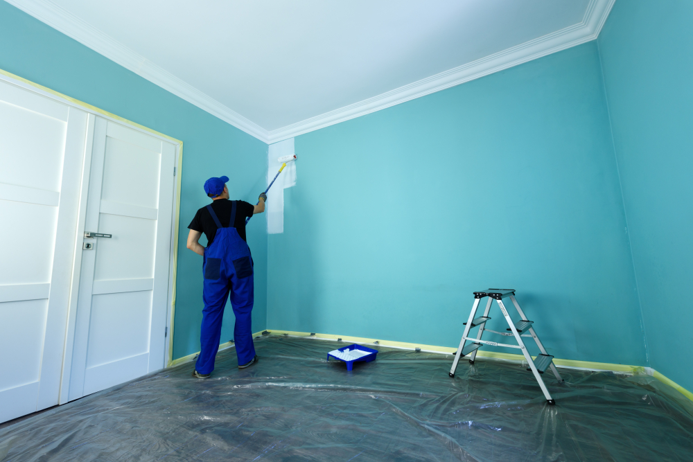 Professional painter applying white paint to a blue interior wall with a roller, showcasing high-quality interior painting services.