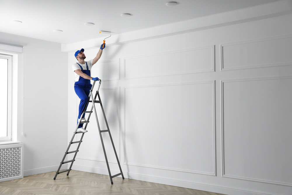 Professional painter standing on a ladder using a roller to paint a white wall, demonstrating how to paint a room like a pro with clean technique.
