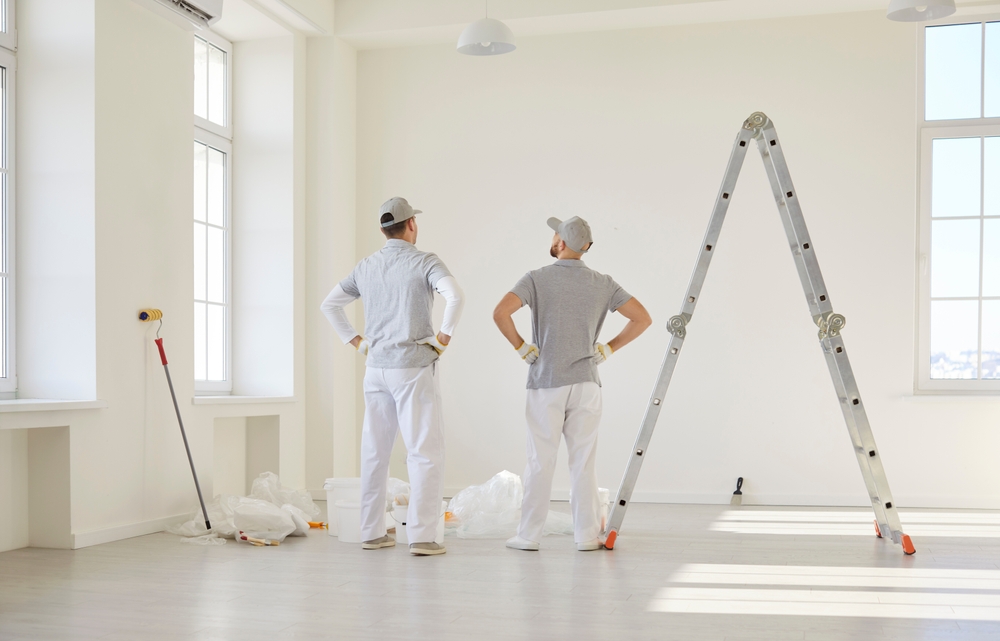 Two professional painters inspecting a freshly painted room with tools and ladder nearby, illustrating how to hire a painting contractor and evaluate quality work.